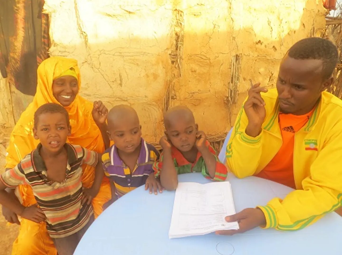 Field staff member reviewing a form at a table with a woman and three young children