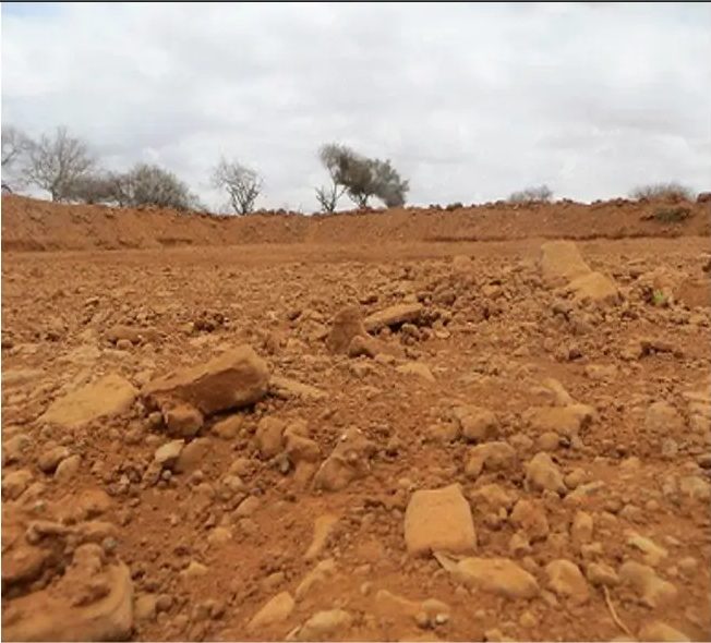 Rubble-strewn red earth basin broken up by loose stones and dry clods