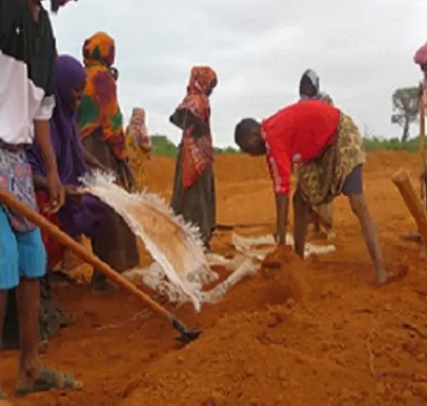 Villagers with hand tools spreading sheeting and moving soil at the catchment edge