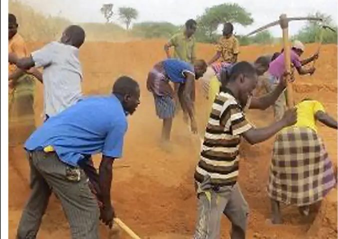Men and women swinging picks in a cloud of dust along a new trench line