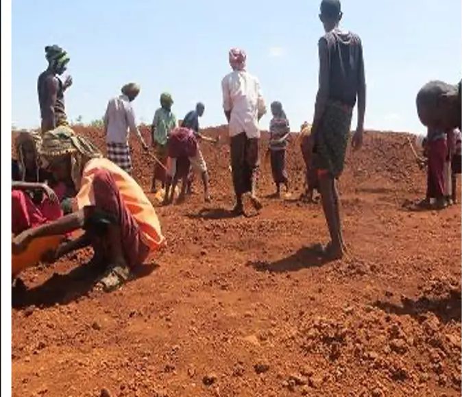 Villagers working shoulder to shoulder on a bank of loose red soil