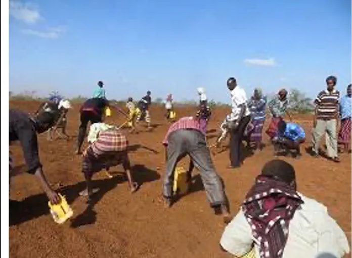 Group carrying jerrycans and tools across an open earthworks site