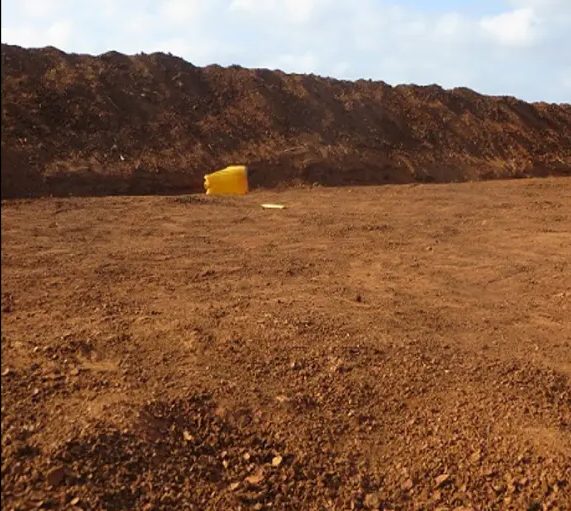 Completed earth bund curving around a levelled catchment floor, a jerrycan left at its base