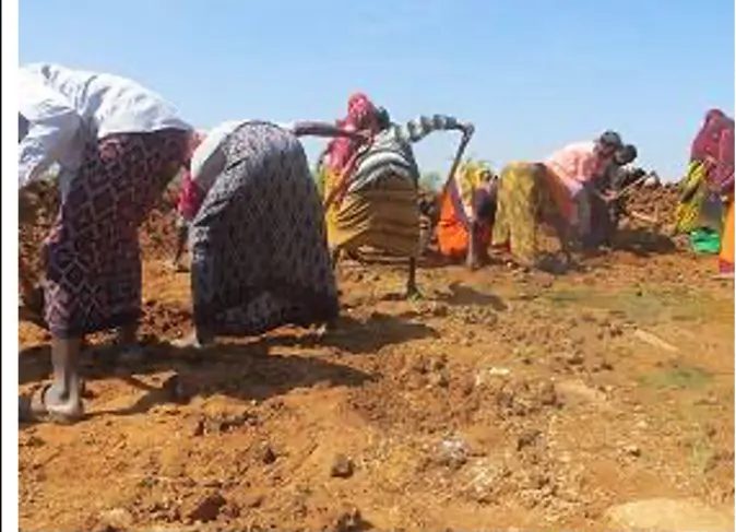 Women in patterned dress lifting soil with hand tools along the excavation line