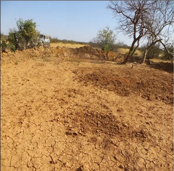 Newly heaped earth bund holding back the deepened basin, trees behind